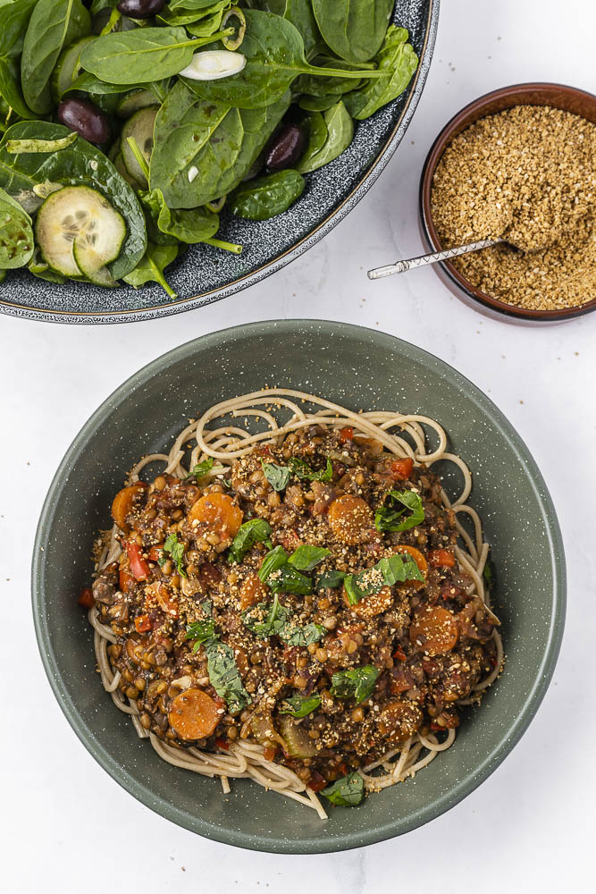 Bovenaanzicht van een bord met vegan spaghetti bolognese met spinaziesalade en vegan parmezaanse kaas