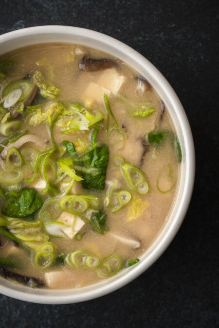 Bovenaanzicht van kom met vegan misosoep. Tofu, spinazie, chinese kool, shii take en bosui maken samen met de miso en bouillon een fantastische combinatie.