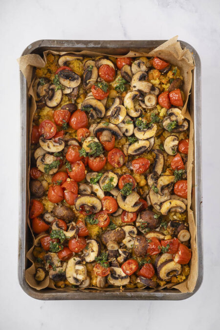 Bovenaanzicht van braadslede met daarin polenta uit de oven met zoete aardappel en lupinebonen. Ook te zien is een topping van champignons en kerstomaatjes.
