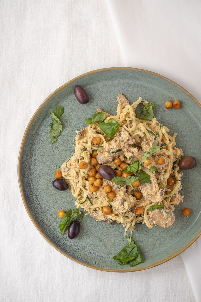 Bovenaanzicht van een bord met courgette spaghetti met gemarineerde champignons, kikkererwten en olijven.